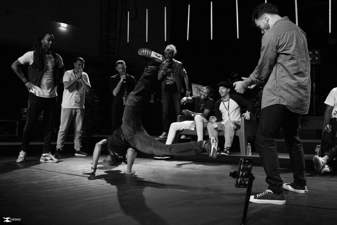 Image en noir et blanc. Un danseur en mouvement a sol au centre. Des danseurs qui le regardent autour. Image en noir et blanc. Un danseur en mouvement a sol au centre. Des danseurs qui le regardent autour.