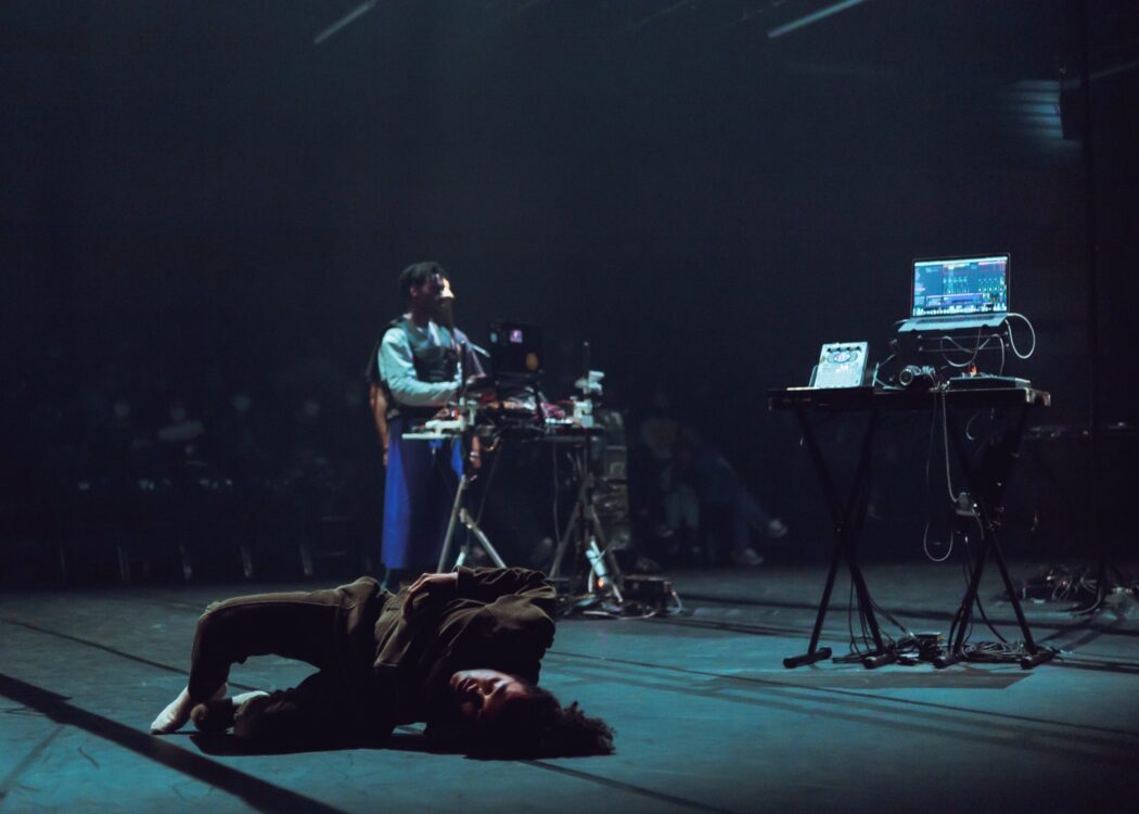Danseur en mouvement au premier plan avec un musicien et le public en fond durant le spectacle Earthbound. Danseur en mouvement au premier plan avec un musicien et le public en fond durant le spectacle Earthbound.