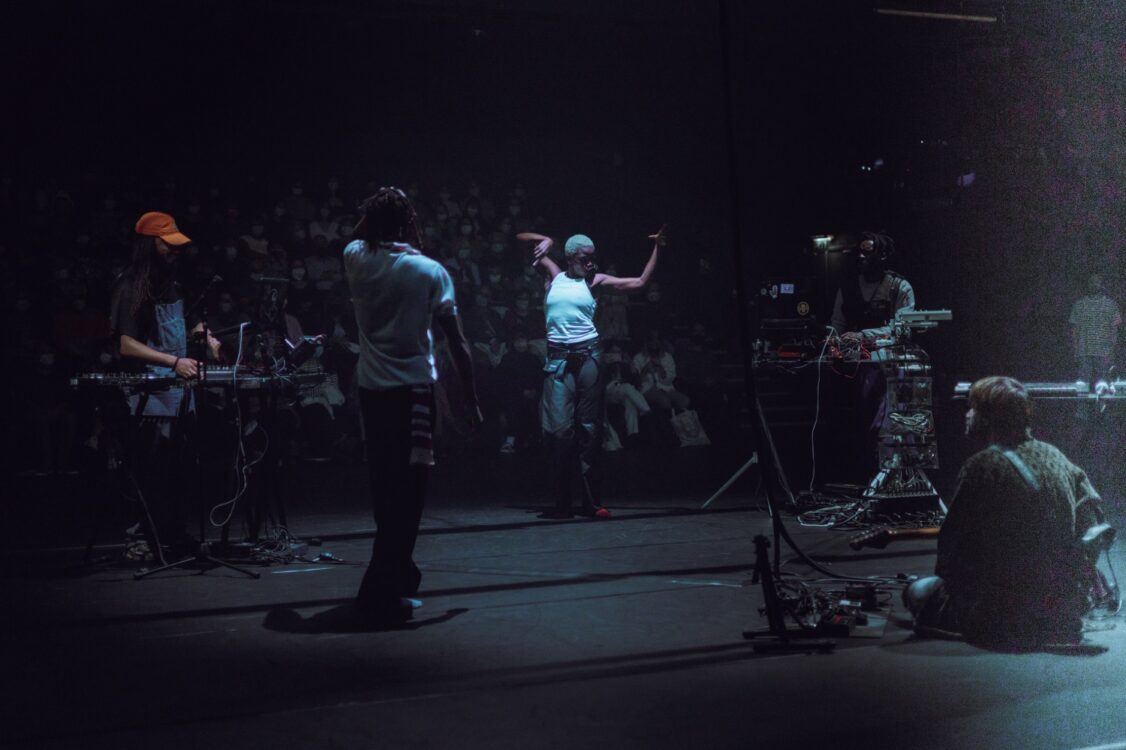 Danseuse en mouvement au centre, musiciens jouant et spectateurs en fond. Danseuse en mouvement au centre, musiciens jouant et spectateurs en fond.