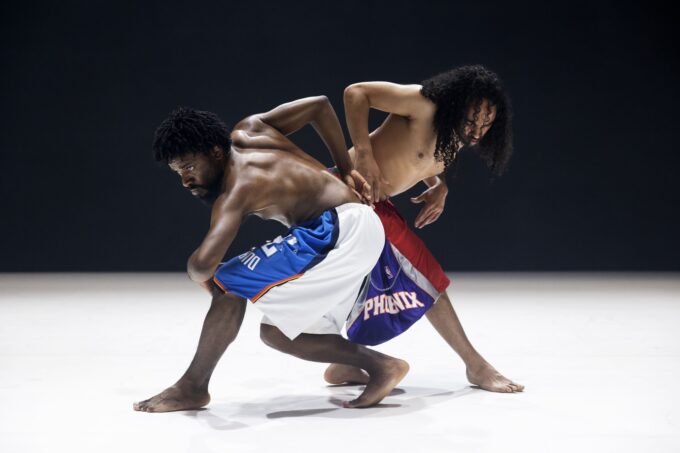 Deux danseurs en mouvement, leurs corps sont côte à côte un qui regarde droit devant lui.