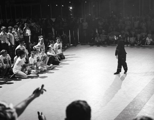 Photo en noir et blanc. Un enfant sur le devant face à d'autres qui danse durant une des battle.