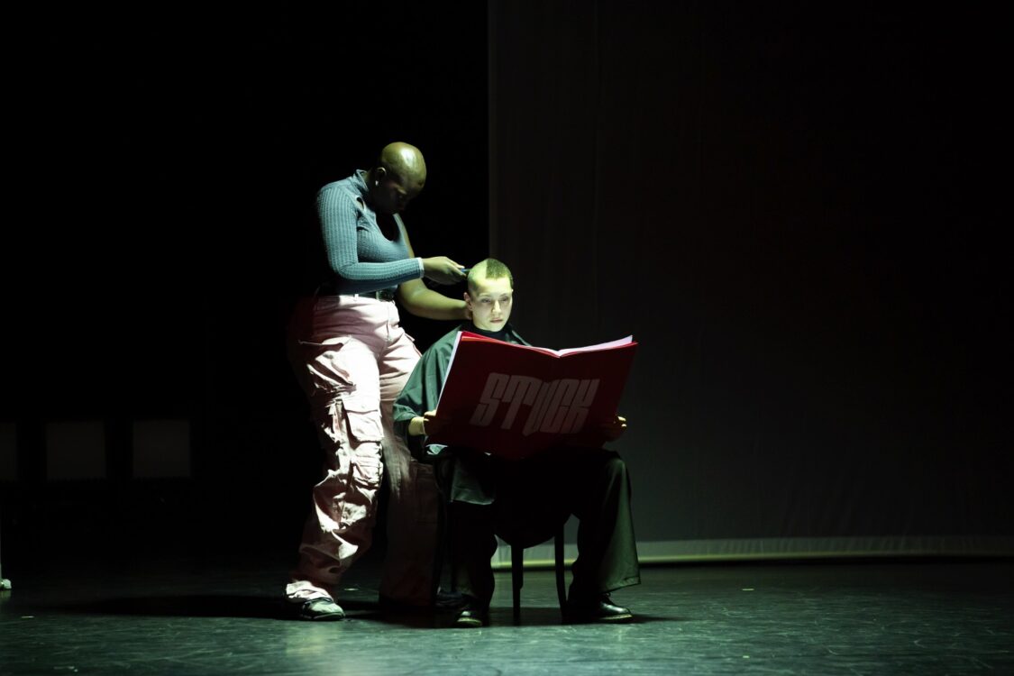 Danseuse rasant une autre assise sur une chaise et lisant un grand magazine Stuck. Danseuse rasant une autre assise sur une chaise et lisant un grand magazine Stuck.