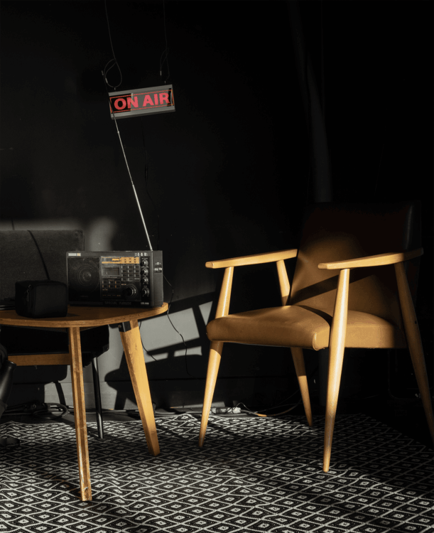 Photo dune chaise avec une table basse et une radio. En fond on peut apercevoir un écran affichant 